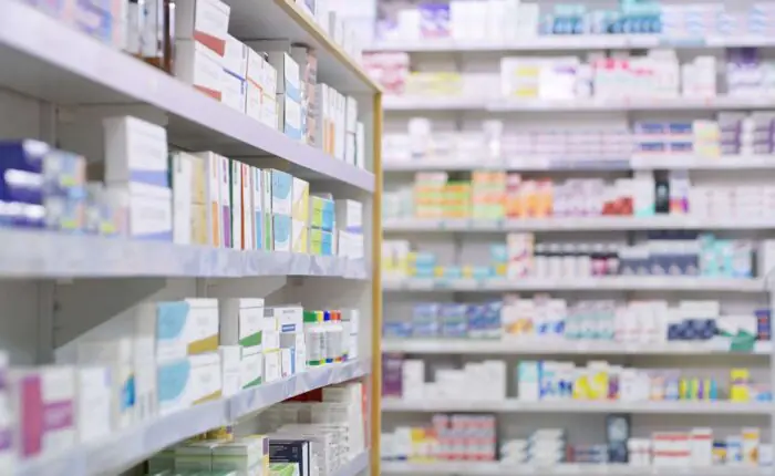 Rows of shelves stocked with medicine boxes and bottles in a pharmacy, with the foreground shelf in sharp focus and the background shelves blurred