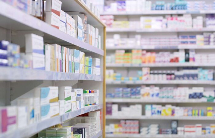 Rows of shelves stocked with medicine boxes and bottles in a pharmacy, with the foreground shelf in sharp focus and the background shelves blurred