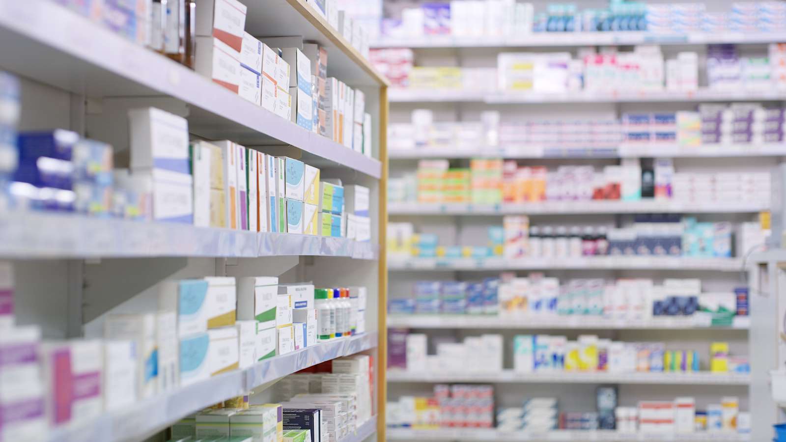 Rows of shelves stocked with medicine boxes and bottles in a pharmacy, with the foreground shelf in sharp focus and the background shelves blurred